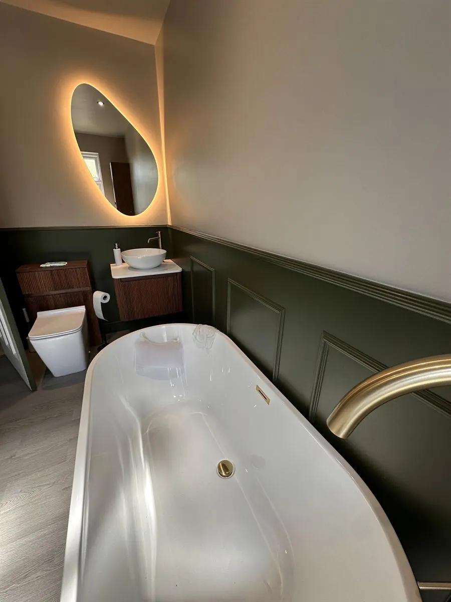 Bathroom renovation with freestanding bath, green panelling and backlit mirror