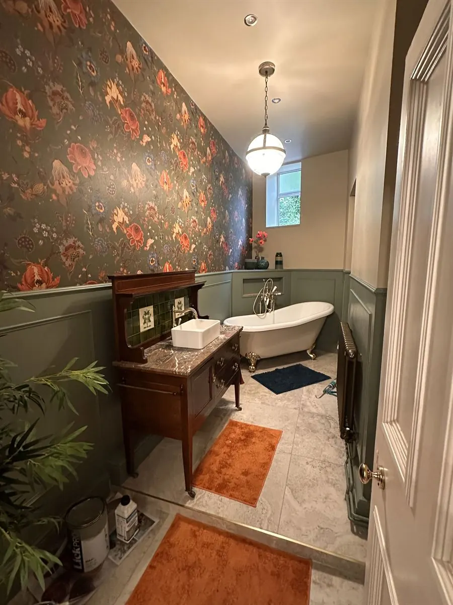 Period bathroom renovation with floral wallpaper and roll-top bath